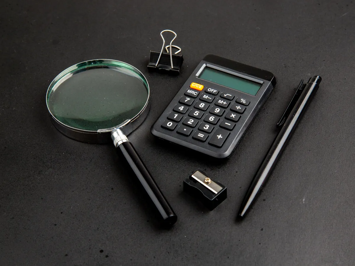 Magnifying glass, calculator and pen on a dark surface